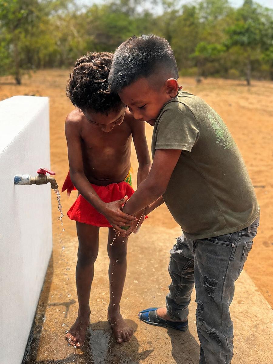 Dos niños lavándose las manos en un grifo comunitario